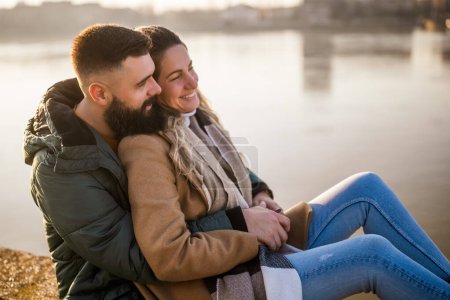 Photo for Happy couple embracing while  enjoy sitting by the river. - Royalty Free Image