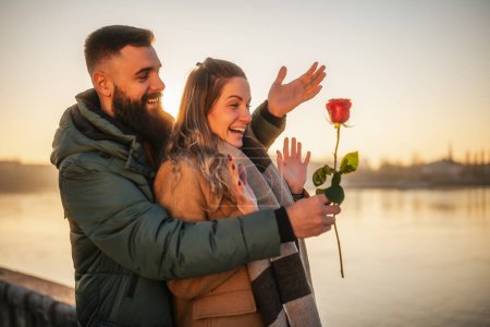Foto de Hombre feliz dando rosa roja a su mujer mientras disfrutan pasar tiempo juntos en una puesta de sol. - Imagen libre de derechos