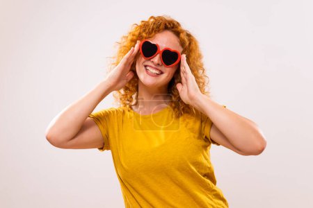 Foto de Imagen de mujer jengibre feliz con gafas de sol en forma de corazón rojo. - Imagen libre de derechos