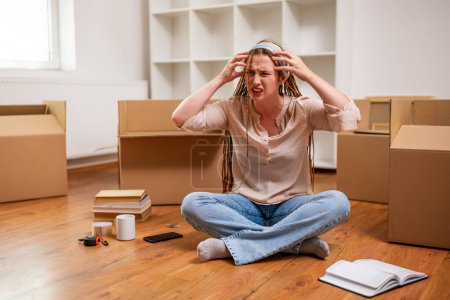 Photo for Angry ginger woman with braids shouting while sitting on the floor in her new apartment. She is exhausted of moving . - Royalty Free Image