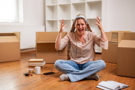 Photo for Angry ginger woman with braids shouting while sitting on the floor in her new apartment. She is exhausted of moving . - Royalty Free Image