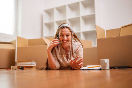 Foto de Mujer de jengibre moderna con trenzas hablando por teléfono mientras se muda a su nuevo apartamento. - Imagen libre de derechos