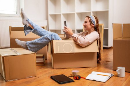 Photo for Happy woman using phone and having fun while moving into new apartment. - Royalty Free Image