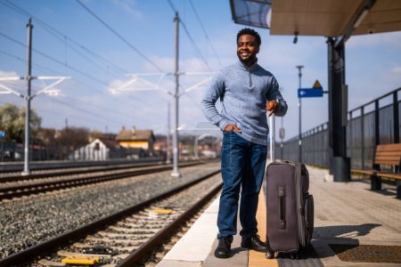 Foto de Hombre feliz con la maleta de pie en la estación de tren. - Imagen libre de derechos