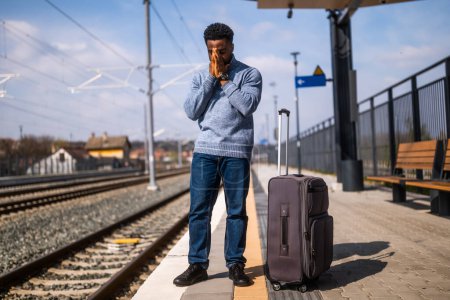 Foto de Hombre preocupado con una maleta de pie en una estación de tren. - Imagen libre de derechos