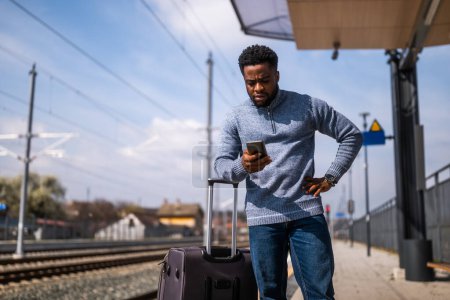 Téléchargez les photos : Un homme choqué avec une valise et un téléphone portable debout sur une gare. - en image libre de droit
