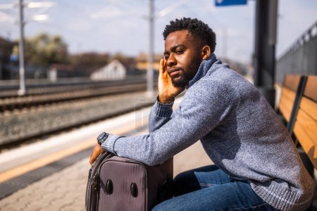 Téléchargez les photos : Homme inquiet avec une valise assise sur un banc à la gare. - en image libre de droit
