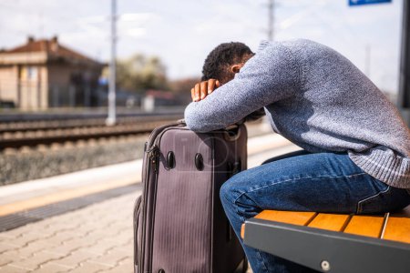 Téléchargez les photos : Homme inquiet avec une valise assise sur un banc à la gare. - en image libre de droit