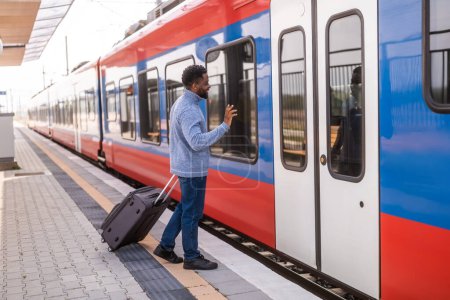 Téléchargez les photos : Homme heureux avec valise entrant dans le train et saluant sur la gare. - en image libre de droit