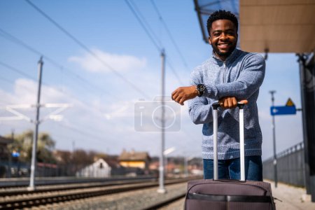 Téléchargez les photos : Homme heureux avec valise debout sur la gare. - en image libre de droit