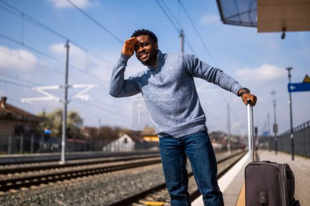 Foto de Hombre feliz mirando hacia otro lado mientras está de pie en una estación de tren. - Imagen libre de derechos