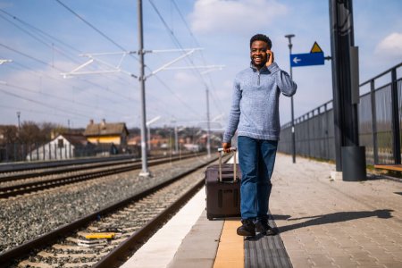Foto de Hombre feliz con una maleta está hablando por teléfono mientras camina en la estación de tren. - Imagen libre de derechos