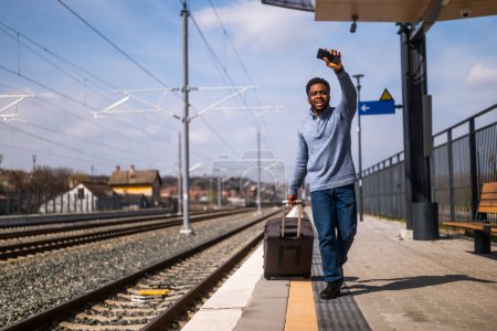 Téléchargez les photos : Homme saluant un train partant et courant le long de la gare avec valise et téléphone portable. - en image libre de droit