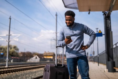 Téléchargez les photos : Homme en colère avec une valise et un téléphone portable debout sur une gare. - en image libre de droit