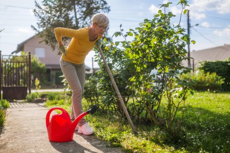 Müde Seniorin hat Rückenschmerzen bei Gartenarbeit in ihrem Garten.