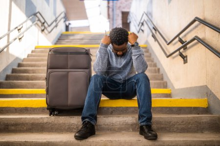 Téléchargez les photos : Homme inquiet avec un téléphone et une valise assis sur un escalier à la gare. - en image libre de droit