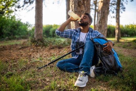 Foto de Joven excursionista bebiendo bebida energética mientras disfruta descansando en la naturaleza. - Imagen libre de derechos