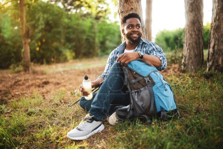 Téléchargez les photos : Jeune randonneur boire boisson énergétique tout en appréciant se reposer dans la nature. - en image libre de droit