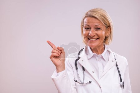 Photo for Portrait of mature female doctor pointing on gray background. - Royalty Free Image