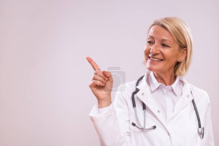 Photo for Portrait of mature female doctor pointing on gray background. - Royalty Free Image