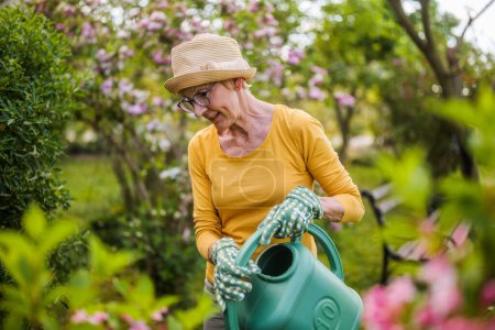 Photo for Happy senior woman enjoys watering plants in her garden. - Royalty Free Image