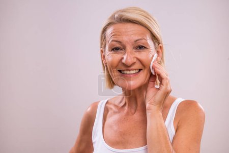 Portrait of beautiful mature woman  cleaning her face with cotton pad.