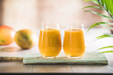 Two mango lassi or kesar milk in glasses. Indian healthy ayurvedic cold drink with mango. Freshness lassi made of yogurt, water, spices, fruits and ice.