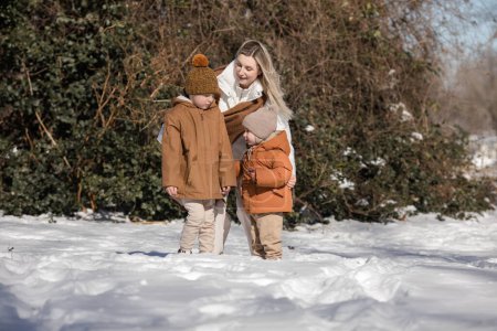 Outdoor family activities for happy winter holidays. Happy mother and two sons playing snowballs on snowy street in suburb. Happy family on winter weekend, Christmas holidays