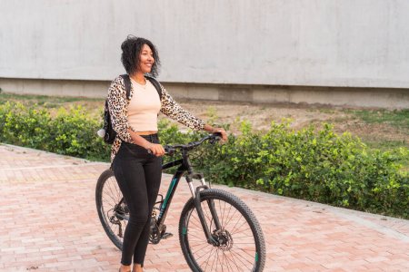 A happy young woman holding her bicycle handlebar, dressed in a fashionable leopard print cardigan.