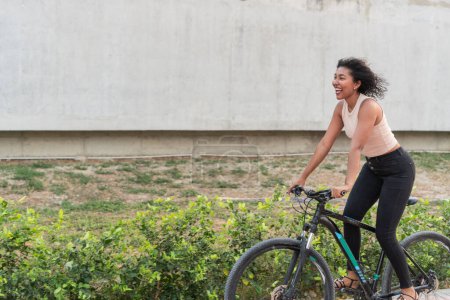 An exuberant young woman with a bright smile rides her bicycle along a serene path.
