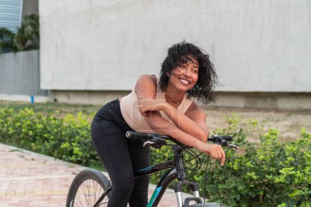 A cheerful young cyclist with a bright smile leans on her bicycle, enjoying a break during her ride.