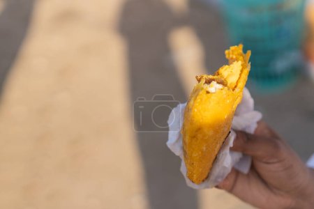 Close-up of a hand holding a freshly cooked empanada with a blurred street background.