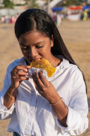 Young woman enjoys eating a crispy empanada outdoors.