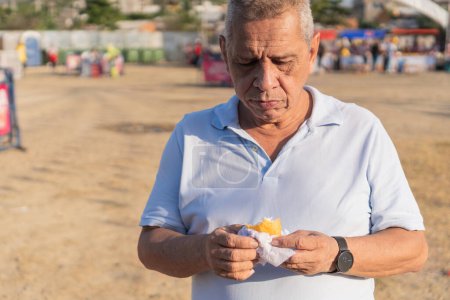 Téléchargez les photos : Un homme mûr goûte une empanada traditionnelle dans un stand de nourriture de rue. - en image libre de droit