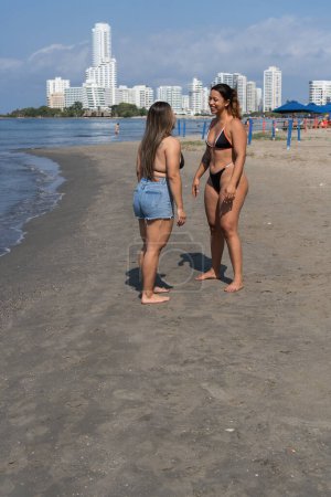 Two friends engage in a lively chat with the city skyline behind them on the beach.