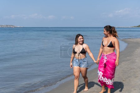Two women share a laugh while walking along the beach.