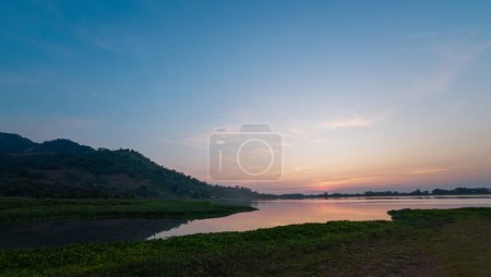 Gentle pastel hues of sunset over a quiet lake with rolling hills and a clear reflection on the water.