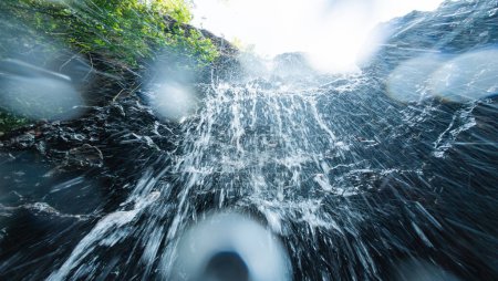 Eine immersive Perspektive von Wasser, das an einem üppigen Wasserfall über die Kameralinse runterrauscht.