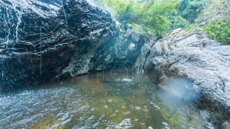 A secluded rock pool fed by a small, glistening waterfall in a lush forest.