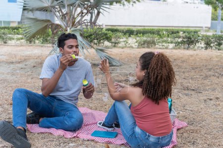 Couple blowing bubbles together on a picnic blanket, enjoying a fun moment.
