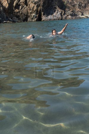A person gestures in the water while swimming with a friend in the sea.