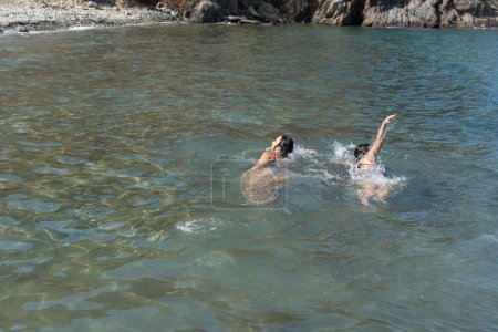 Two swimmers enjoy the clear sea, with rocky shores in the distance.