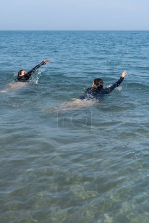 Zwei Personen schwimmen freudig im Meer, Arme in Bewegung.
