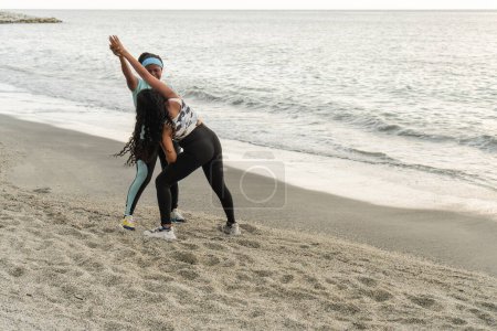 Two athletic women engaging in stretching exercises on a tranquil beach.