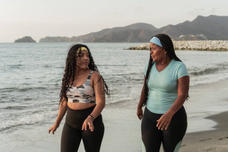 Deux femmes prennent une pause de leur séance d'entraînement à la plage, contemplant la vue sur l'océan.