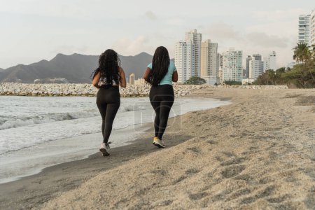 Two women running on a beach with the city skyline in the background.