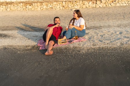 Paar genießt Wein und Gespräch am Strand bei Sonnenuntergang.