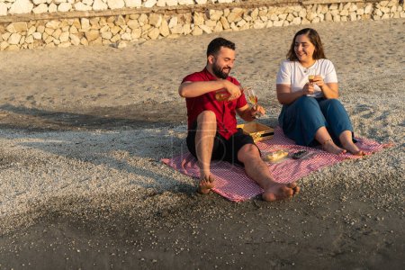 Relaxed couple sharing a drink and a laugh on a beach blanket