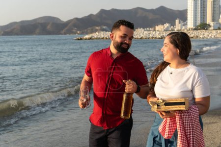 A couple cheerfully toasts on the beach with city mountains in the background