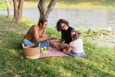 Fröhliche Familie bei einem Imbiss auf einer Picknickdecke am ruhigen Seeufer.